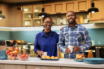 Portrait of african american couple at home preparing to serve homemade pastry and coffee at kitchen countertop. Smiling man and woman expressing love and a balanced relationship, proteins.