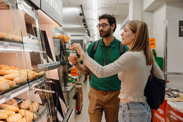 A man and a woman stand and choose pastries while holding their hands towards the counter