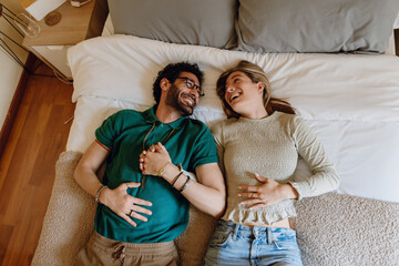 A man and a woman are holding hands and lying on a bed while laughing and looking at each other