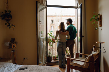 A man and a woman are standing at the entrance to a balcony and he is hugging her