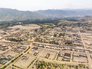 Aerial panoramic view of urban expansion in the Cieneguilla valley near Lima Peru showing residential neighborhoods and green areas surrounded by arid mountains.