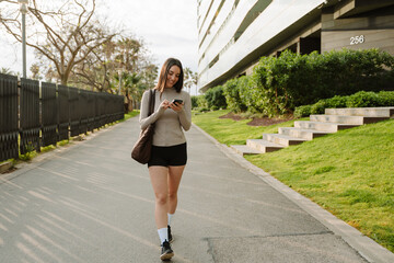A female athlete walks and looks at the phone she is holding while smiling