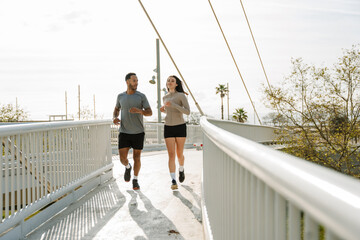 A male athlete talks to a female athlete while they run on a bridge