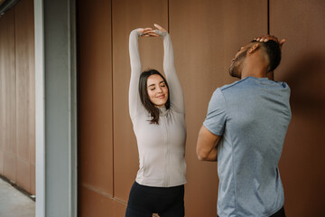 A female athlete stretches her arms above her head with her eyes closed while standing opposite a...