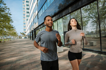 Male and female athletes running near building and looking ahead