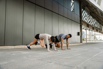 A male athlete laughs and looks at a female athlete next to him as they raise their knees and stand in a push-up position on the ground