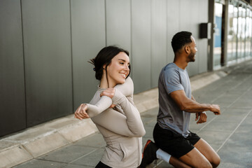Female athlete smiles and stretches her arm while male athlete kneels on the ground next to her