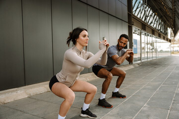 A female athlete looks ahead while a male athlete looks at her while they hold their hands in front of them and squat