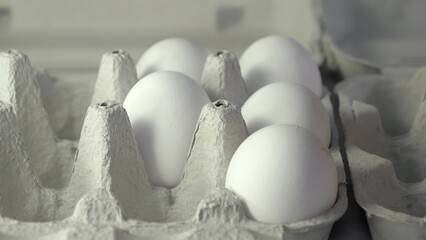 A close-up view of fresh white eggs nestled in a cardboard carton, showcasing their smooth texture and subtle shadows, creating a serene and minimalist atmosphere in the composition