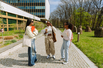 Fototapeta na wymiar A group of three female students stand and hold notebooks and folders while two of them listen to the other one speaking