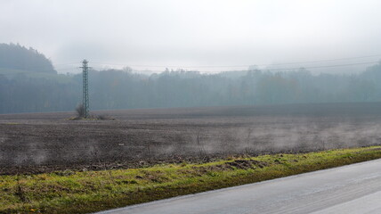 Tilled soil stretches toward a distant treeline. A utility pole stands in the foreground. Mist...