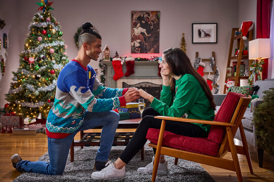 Man proposes to woman in festive living room decorated with Christmas tree and holiday decorations