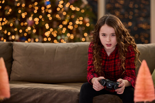 Young girl playing video games with controller in front of Christmas tree lights at home