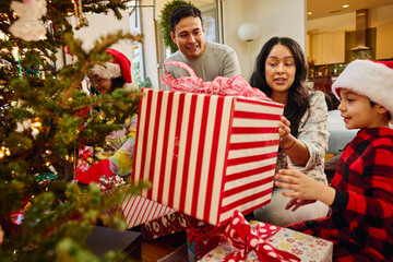 Family opening Christmas presents together by decorated tree in festive home during holiday celebration