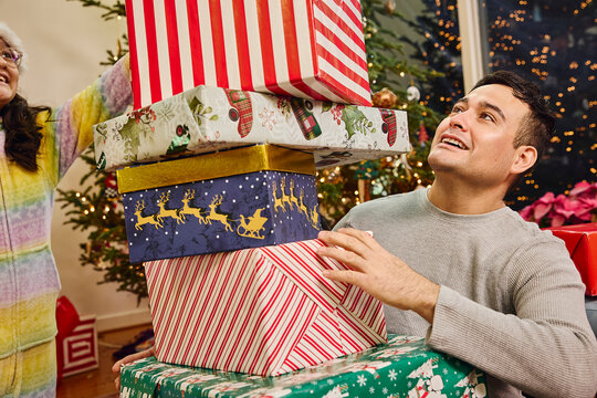 Man holding stack of wrapped Christmas presents in festive holiday decorated living room with tree