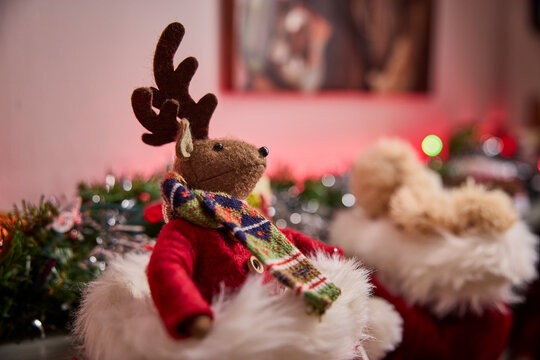 Festive reindeer plush toy in cozy holiday setting with colorful scarf and decorations