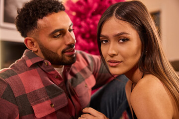 Couple poses together in elegant indoor setting with vibrant pink floral backdrop and warm lighting