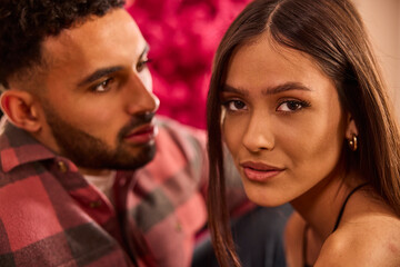 Young couple poses together in romantic portrait with pink floral background and warm lighting