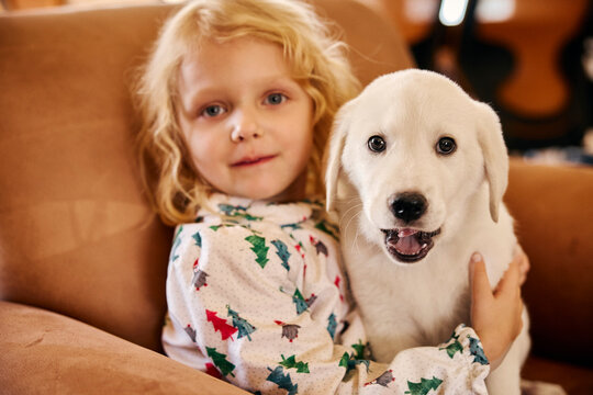 Young child in festive pajamas cuddling with adorable white puppy on cozy couch at home