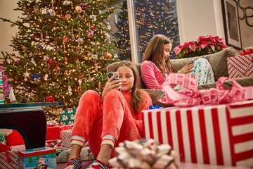 Two girls in pajamas enjoy Christmas morning with presents near a decorated tree and festive lights
