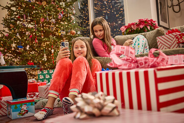 Two sisters in matching pajamas take a selfie on Christmas morning surrounded by presents and decorations