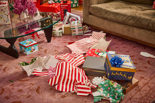 Unwrapped Christmas presents and torn wrapping paper scattered across living room floor on holiday morning