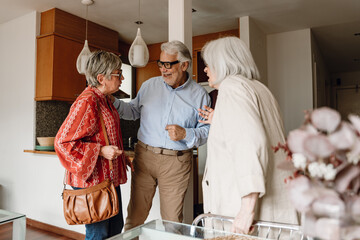 A man smiles and puts his hand on a woman's shoulder while a female friend stands next to them and they talk