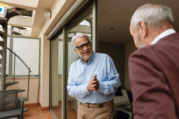 A man rubs his hands and smiles while listening to his male friend across from him