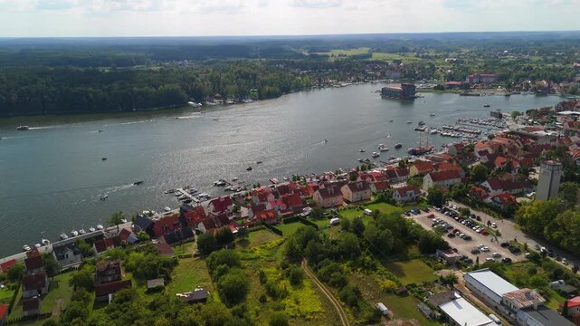 Aerial view of Mikolajki, Masuria showcasing vibrant waterfront houses along the lake, surrounded by lush greenery and sailboats adding life to the serene landscape.