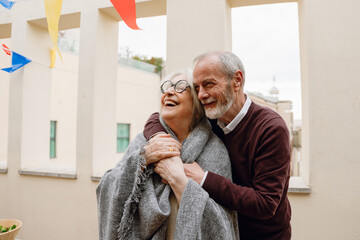 A woman is laughing and putting her hand on the hand of a man who is hugging her from behind and smiling