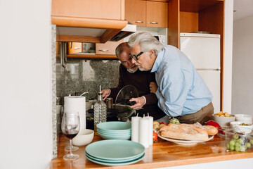 Man holding lid and talking to male friend who is looking into pan