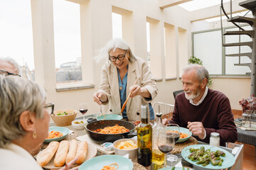 A woman stands and laughs while holding a spatula and fork while a group of three friends sit at a table