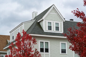A picturesque family house with dormer windows framed by vibrant red autumn trees in the Brighton area of Boston, Massachusetts, USA
