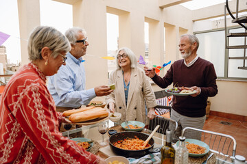 Group of four friends standing at a table laughing while talking and holding plates of food