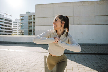 A woman laughs and holds her hands together in front of her while standing on one leg and leaning her foot on a stone stool
