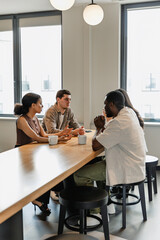 A group of four workers are sitting at a table and talking while looking at each other