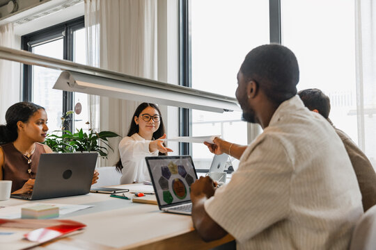 Female and male employees handing over documents while sitting at a table near two other employees