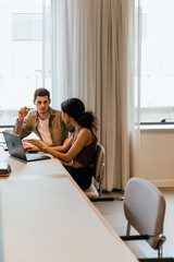 A male worker holds a pencil and listens to a female worker sitting next to him at a desk and...