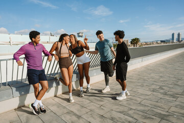 A group of five athletes stand and talk while laughing and four of them lean on the fence