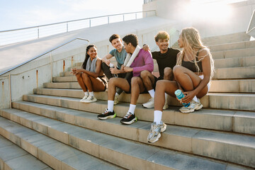A group of five athletes sit on the stairs and laugh while talking and holding bottles