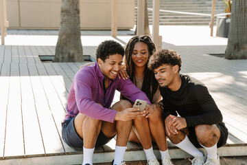 A group of three athletes are sitting and smiling while looking at a phone that one of them is showing