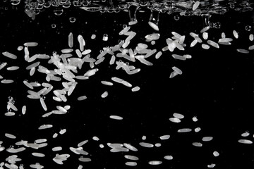 Rice grains falling through water creating bubbles and ripples in a dark setting