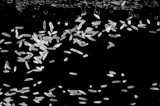 Rice grains falling through water creating bubbles and ripples in a dark setting - Powered by Adobe