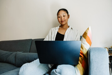 Woman smiling and looking at laptop on her lap while sitting on sofa