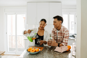 Woman pouring juice from juicer into glass while standing at table next to man and they are smiling