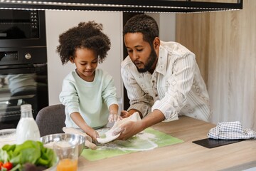 A father and his daughter hold dough and stand at the table while he talks