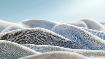 A macro shot of draped, folded blue denim fabric creating abstract shapes and textures. The background is a soft, gradient blue sky with subtle light effects, s