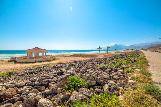 Mughsayl Beach close to Salalah, Oman featuring a red-roofed pavilion, sandy coastline, and palm trees under a clear blue sky, offering a serene coastal landscape for travel and tourism in Dhofar