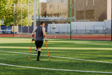 A man stands and holds crutches while looking at a ball in front of his face