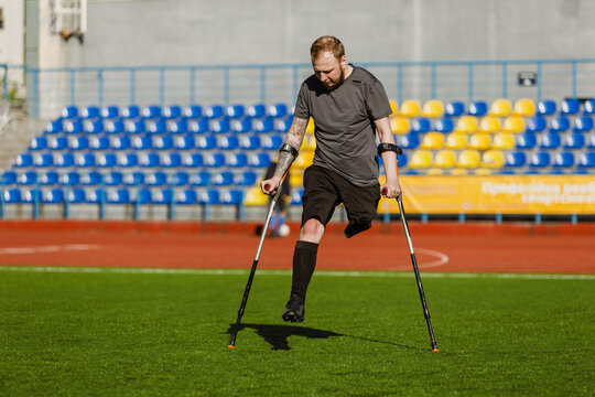 Football player running across the field and leaning on crutches